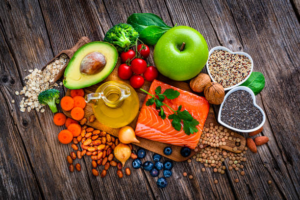 Overhead view of a group of food for heart care and lower cholesterol shot on rustic wooden table. The composition includes salmon, olive oil, chia seeds, quinoa, broccoli, avocado, green apple, oatmeal, spinach, brown lwntil, pinto bean, onion, almonds, walnut, carrot blueberries among others. High resolution 42Mp studio digital capture taken with SONY A7rII and Zeiss Batis 40mm F2.0 CF lens