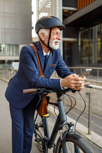 Thoughtful male professional in helmet using phone and looking away while leaning on bicycle in city