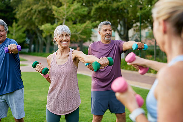 Elderly group of people working out with dumbbells in a park. Mature fitness group of women and men lifting small weights outdoors. Happy active adults in sportswear exercising together with dumbbells.