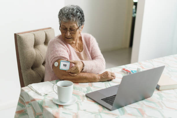 A latin senior woman sitting at home using a medical device for an online consultation with a health professional.