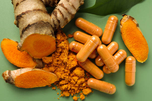 Aromatic turmeric powder, pills and raw roots on green background, flat lay