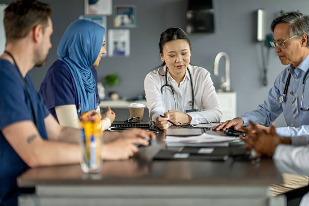 Healthcare professionals gathered around a meeting table, discussing patient care strategies. They collaborate in a contemporary medical environment, focused on providing solutions. Diversity and teamwork emphasize their commitment to excellence.