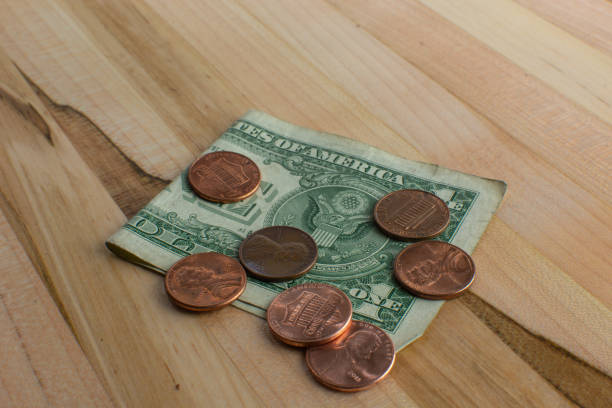 US pennies on top of a folded dollar bill on a wooden table.