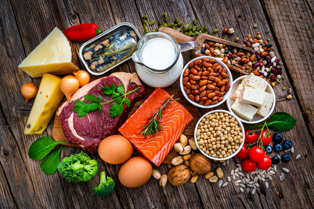 Overhead view of a group of food with high content of healthy proteins shot on rustic wooden table. The composition includes raw beef steak, Salmon steak, walnut, sardines, tofu, soy beans, legumes, milk, eggs, cheese, quinoa, peanut among others. High resolution 42Mp studio digital capture taken with SONY A7rII and Zeiss Batis 40mm F2.0 CF lens